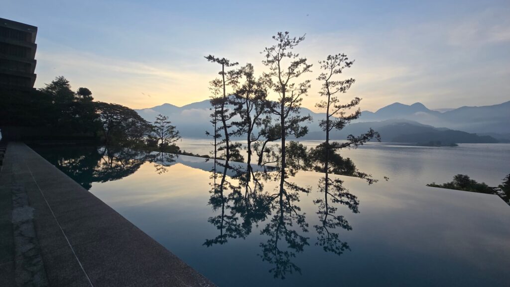 日出時分的涵碧樓無邊際泳池，晨光與山景倒映於平靜水面