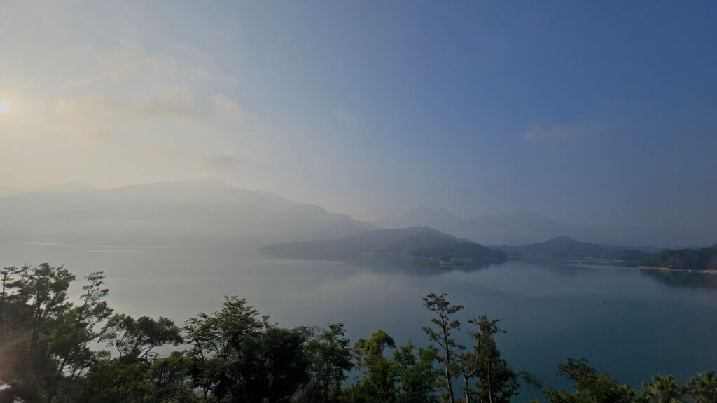 日月潭晨曦中的湖光山色，遠方層巒交疊於薄霧之間